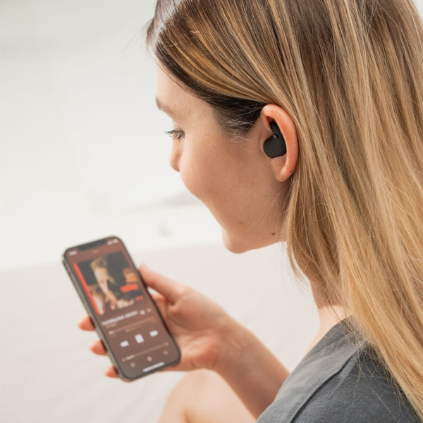 zijkant beeld van een blonde vrouw die op haar smarthphone muziek zoekt en oordopjes in haar oor heeft