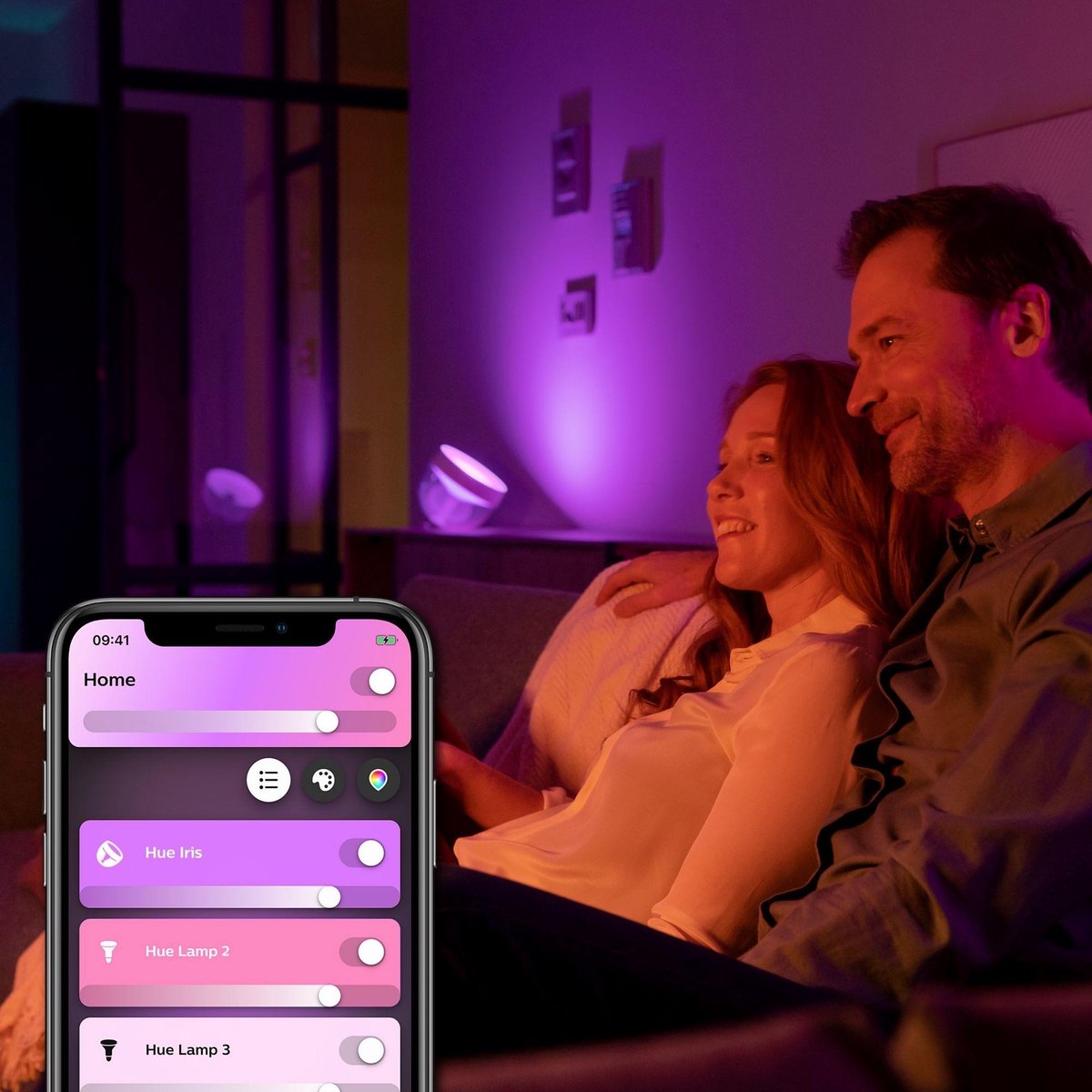 philips hue iris lamp app op een mobiele telefoon met een koppel zittend op de bank op de achtergrond