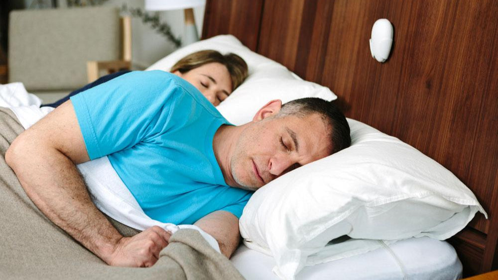 Man en vrouw in bed aan het slapen met een slaahulpmiddel boven op het bedframe